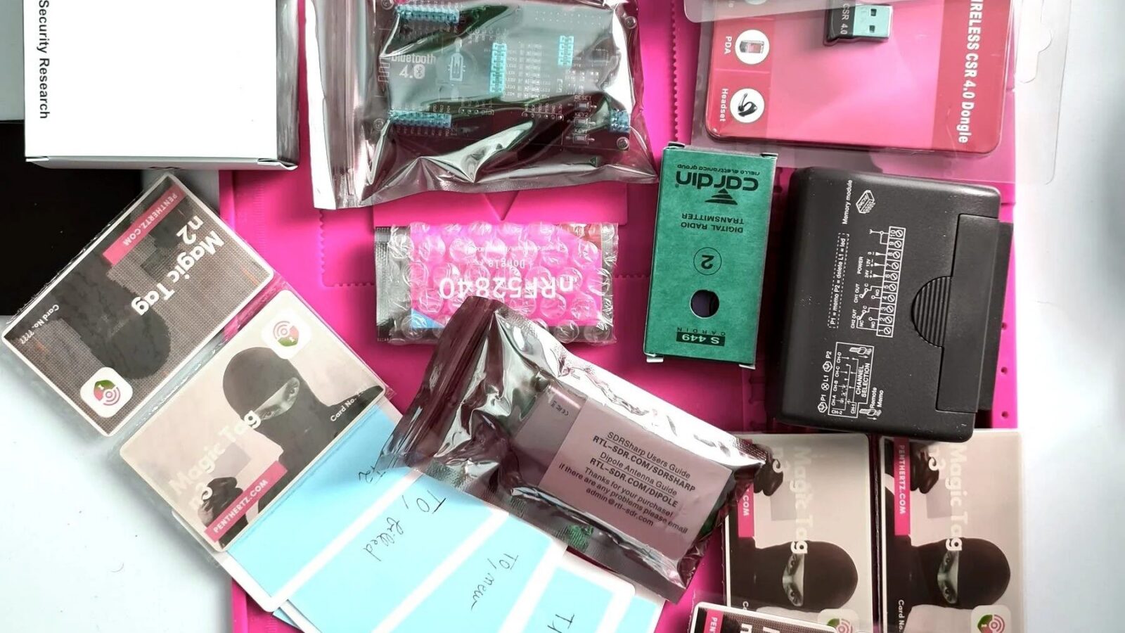 Red Team OTA training kit on a pink ESD mat: Proxmark3 box, Magic Tag cards, blank cards, Bluetooth dongles and targets