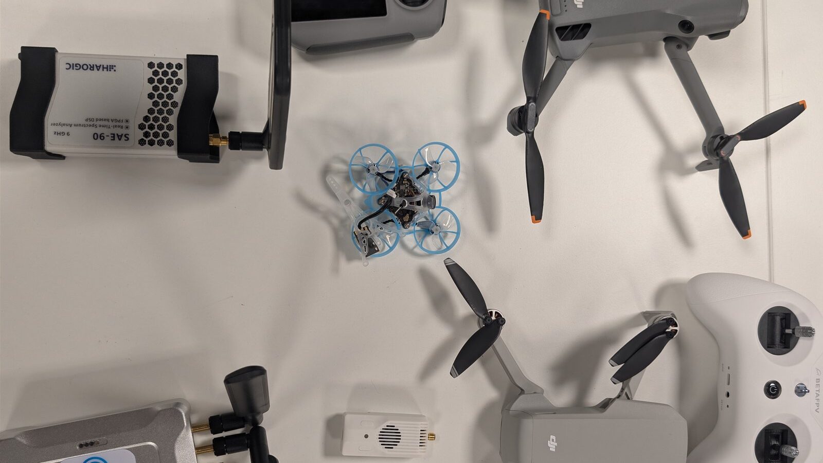 Consumer drones, an FPV racing quad and their controllers on a bench with a spectrum analyser and SDR